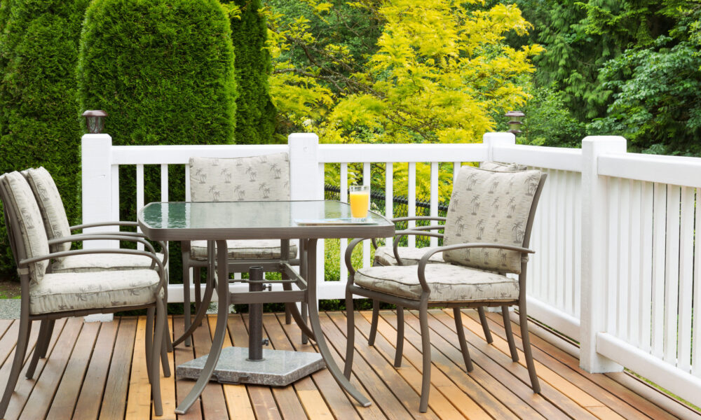 Closeup horizontal photo of outdoor furniture on open cedar patio with seasonal trees in full bloom in background